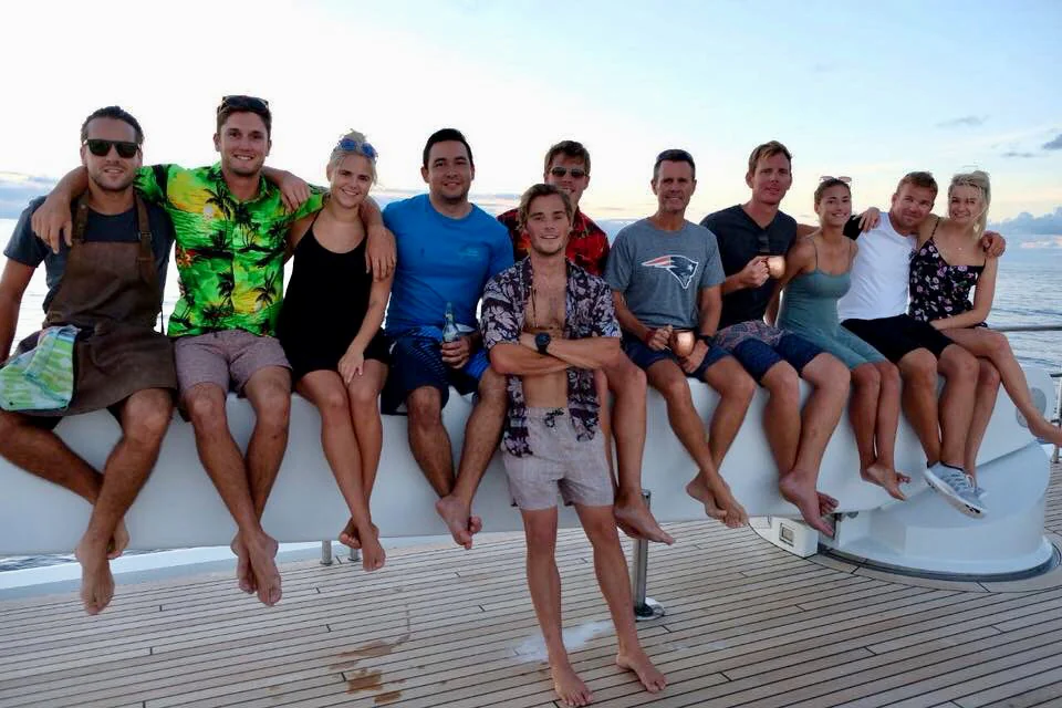 A yacht crew sitting together on the aft rail at sunset