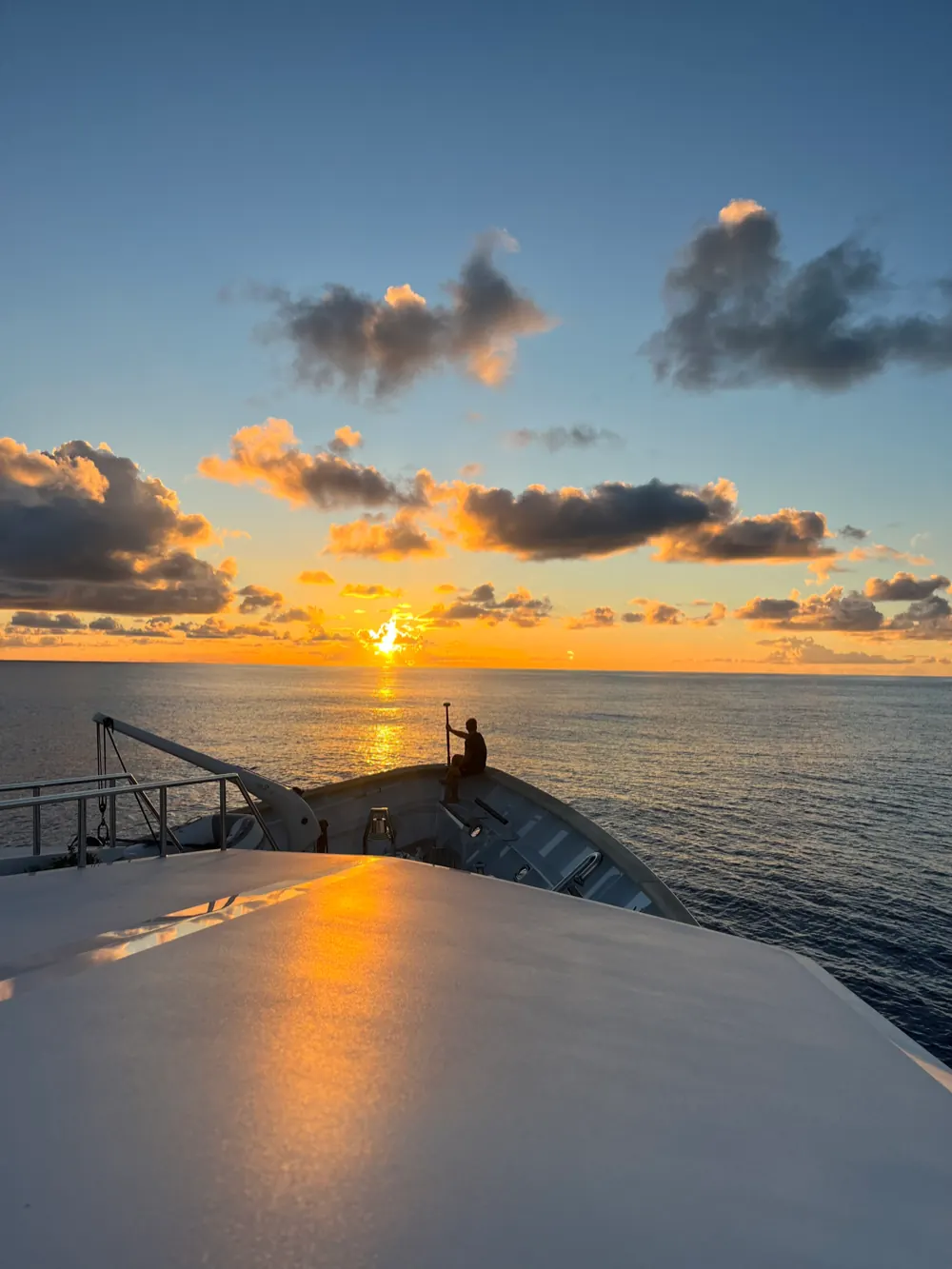 Sunset from a yacht's bow with crew on the foredeck